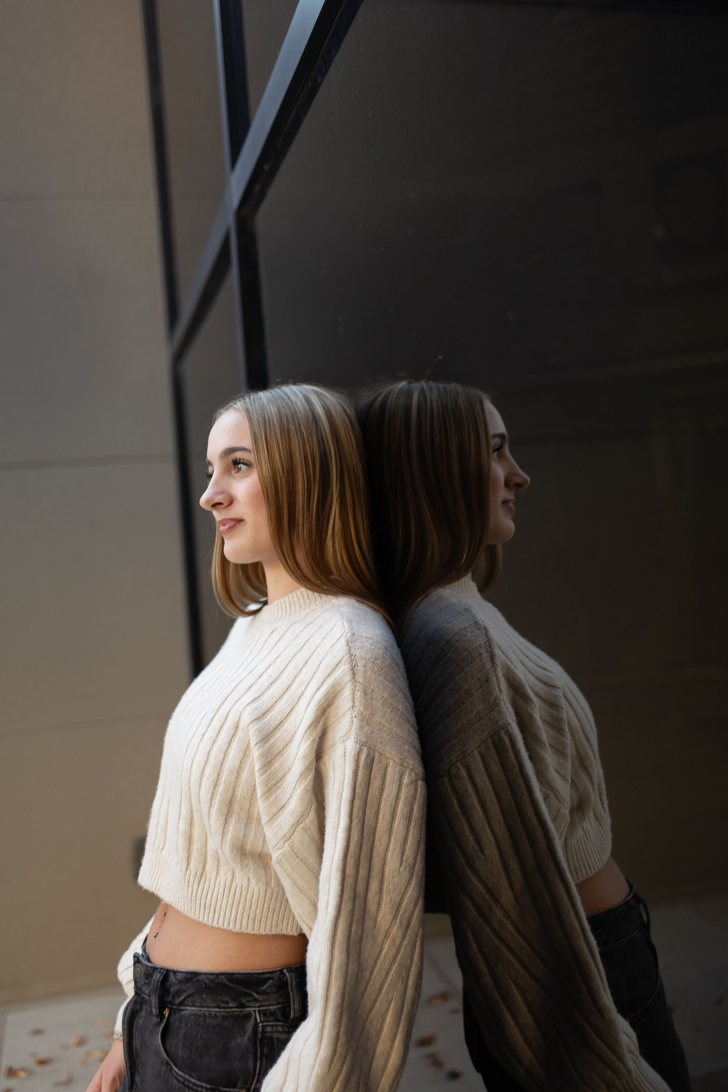 Sioux City, Iowa photographer. young woman in cream knit sweaters standing against dark modern wall.