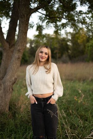 Sioux City, Iowa photographer. Smiling blonde woman in cream ribbed crop sweater and black jeans standing in wooded outdoor setting.