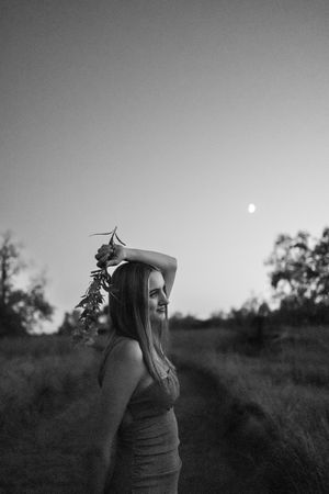 Sioux City, Iowa photographer. Black and white portrait of woman holding wildflowers at dusk with full moon visible in sky.