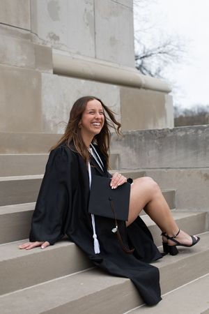 Sioux City, Iowa photographer. Laughing woman in graduation cap and gown sitting on stone steps holding her mortarboard.