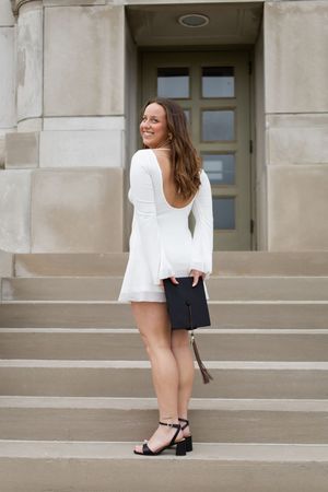 Sioux City, Iowa photographer. Smiling woman in white backless dress holding graduation cap on stone building steps.