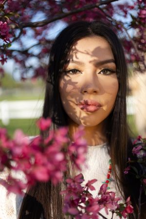 Sioux City, Iowa photographer. Young woman with dark hair framed by pink cherry blossom flowers in soft sunlight.