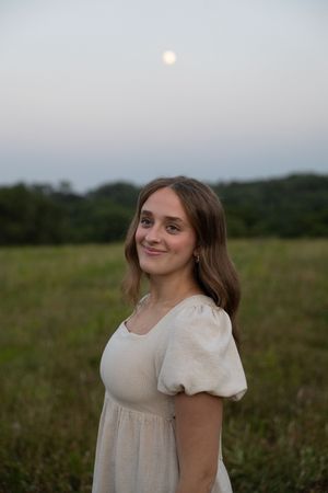 Sioux City, Iowa photographer. Young woman in cream puff-sleeve dress smiles outdoors in field with full moon behind her.