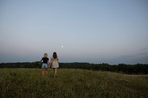 Sioux City, Iowa photographer. Two girls hold hands in open field at dusk with moon visible in twilight sky.