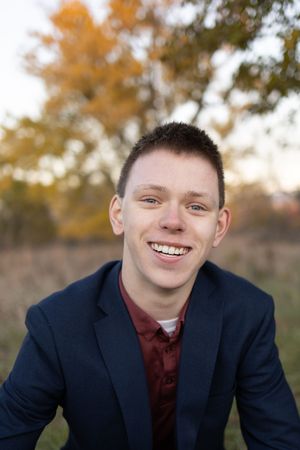 Sioux City, Iowa photographer. A young man in a navy blazer and burgundy shirt smiling outdoors during fall season.