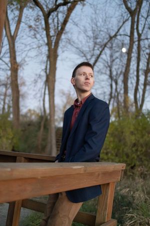 Sioux City, Iowa photographer. A young man in a navy blazer sits at a wooden table outdoors at twilight gazing upward.