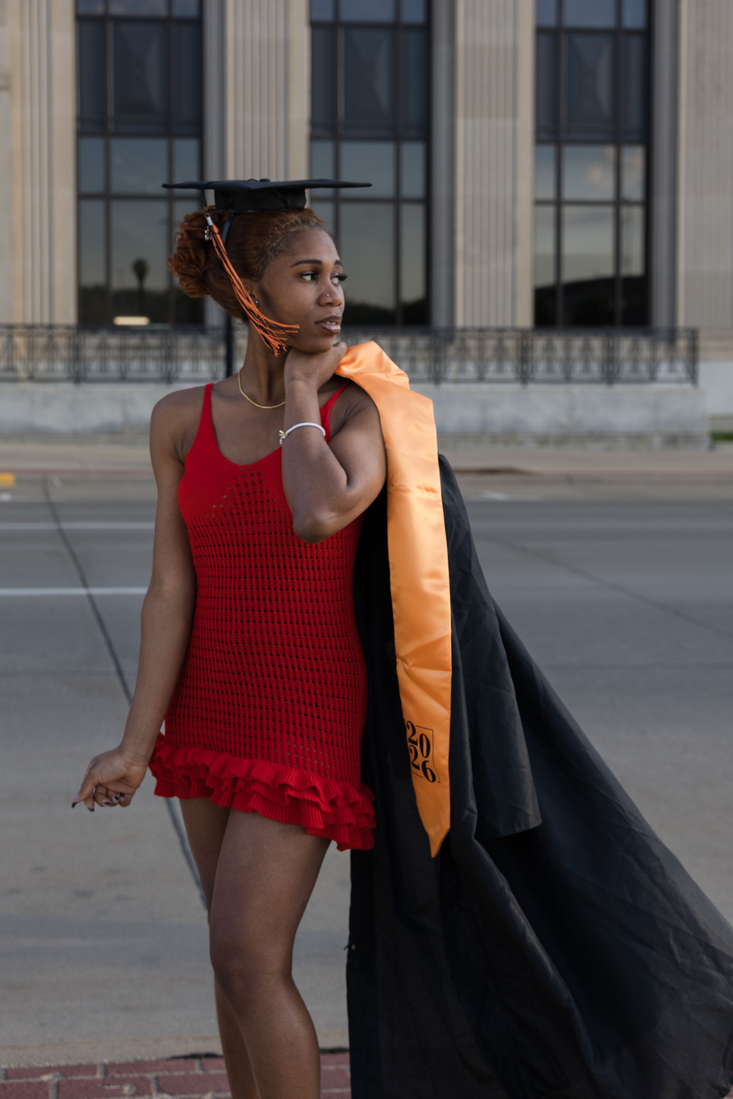 Sioux City, Iowa photographer. Young Black woman in red dress holding graduation cap and gown outdoors.
