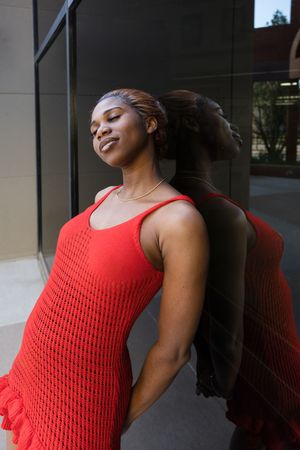 Sioux City, Iowa photographer. Young Black woman in red knit dress leaning against glass building exterior.