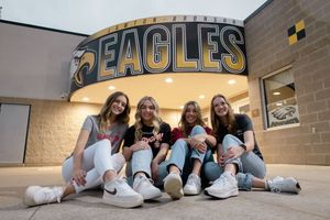 Sioux City, Iowa photographer. Four teenage girls pose together smiling in front of an Eagles school sign at dusk.