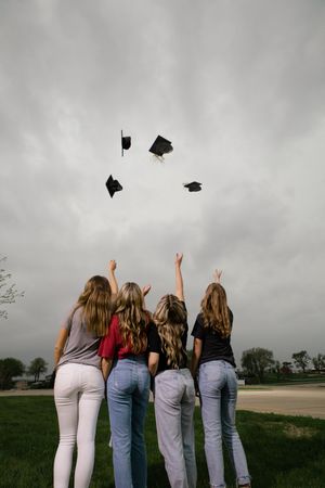 Sioux City, Iowa photographer. Four girls toss graduation caps into a cloudy sky celebrating their high school graduation outdoors.
