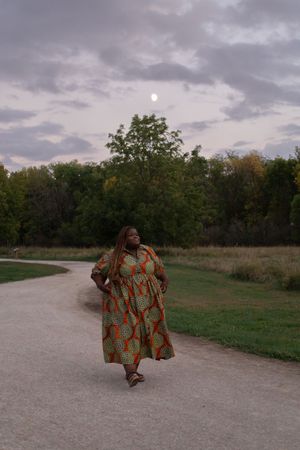 Sioux City, Iowa photographer. Woman in vibrant African print dress walking on a park path at dusk with full moon visible.