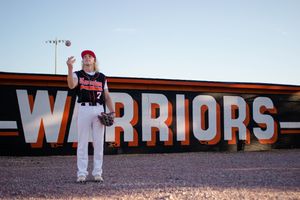 Sioux City, Iowa photographer. A young baseball player tosses a ball in front of a large Warriors sign at dusk.