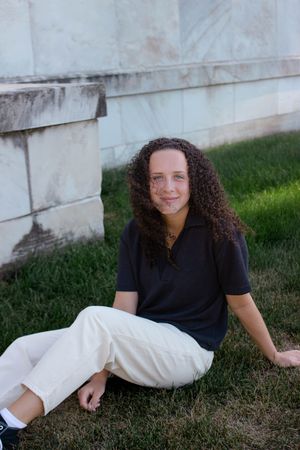 Sioux City, Iowa photographer. A teen with curly hair sits on green grass against a marble wall smiling at the camera.