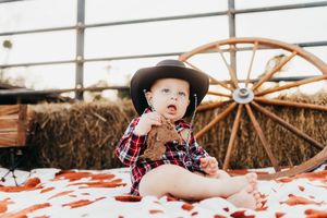 A small child in a plaid shirt sits on a white blanket with red paint creating messy artwork.