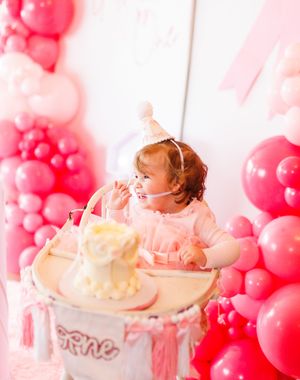 Pink balloon arch decorates a whimsical birthday celebration with cake and party decor in soft rosy hues.