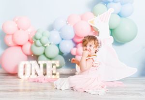 Toddler girl in pink dress celebrates first birthday with colorful balloon arch and ONE sign.