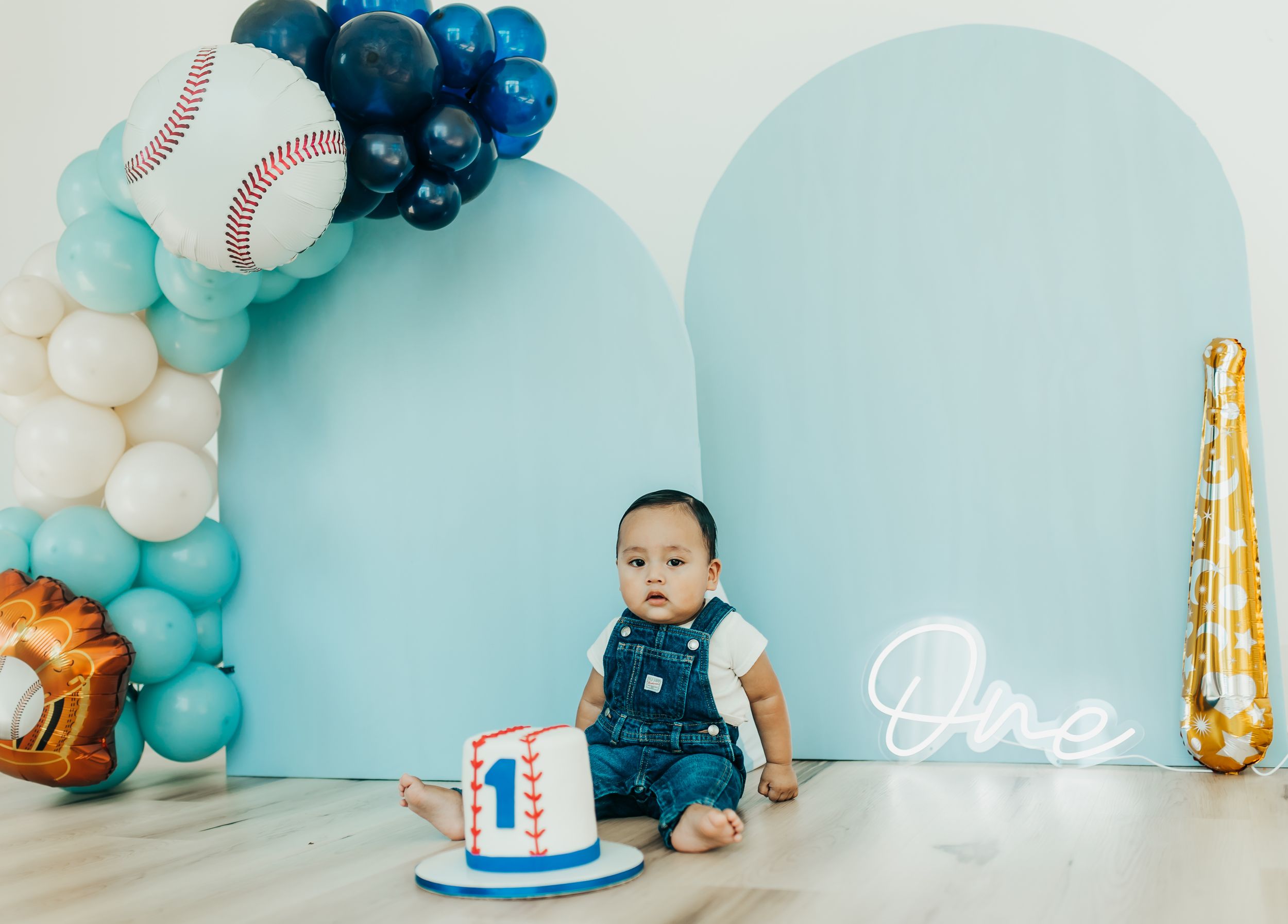 Baseball themed first birthday party setup with blue and white balloon garland and decorative arches.
