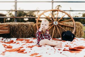 Couple sitting on a red and white blanket surrounded by hay bales at a rustic outdoor setting.