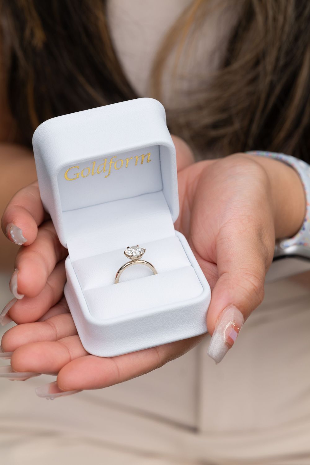Woman holding an open white ring box displaying a solitaire diamond engagement ring from Gallagher's.