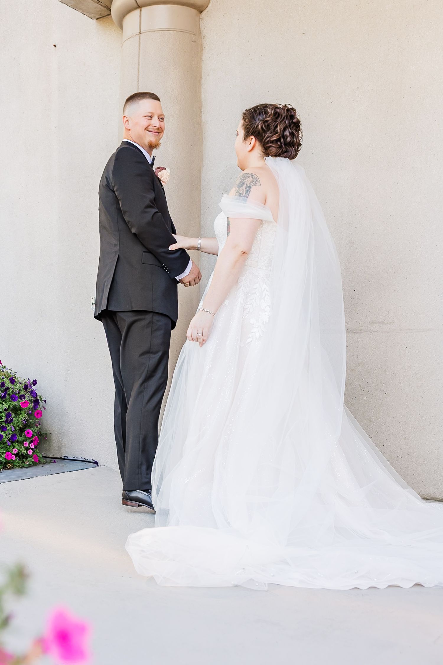A series of four photos showing a bride and groom having a first look moment in a light-colored hallway with pink flowers.