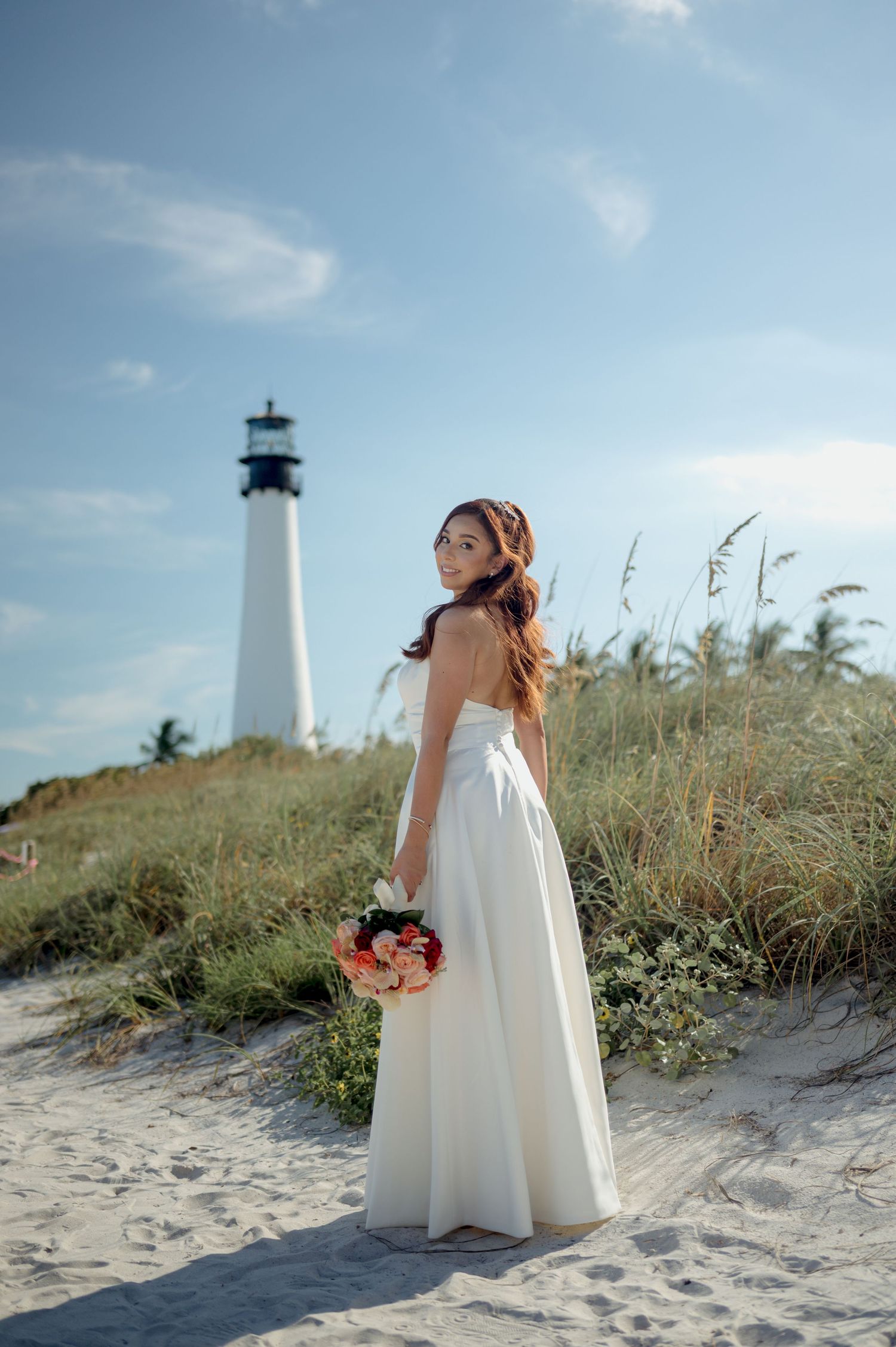 A lighthouse stands tall on a sandy beach dune with sea grass swaying in the breeze.
