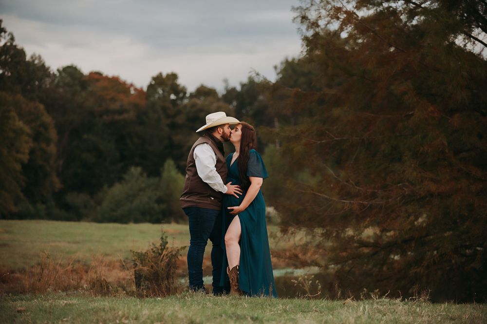 A couple in western attire embraces in a romantic autumn field during golden hour.