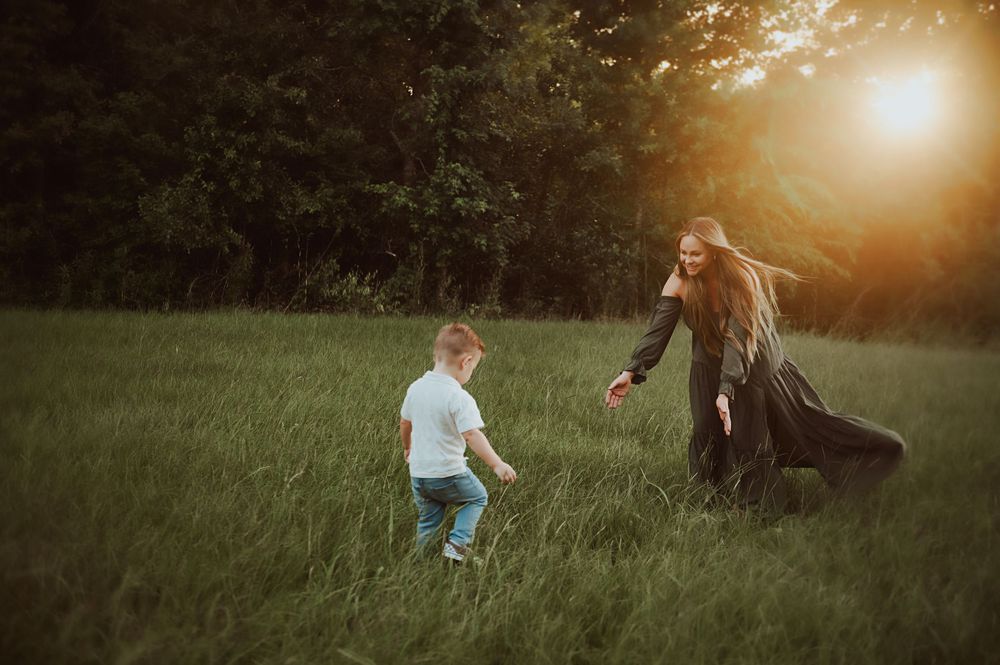 Mother and child playing in a sunlit green meadow at golden hour, with trees in the background.