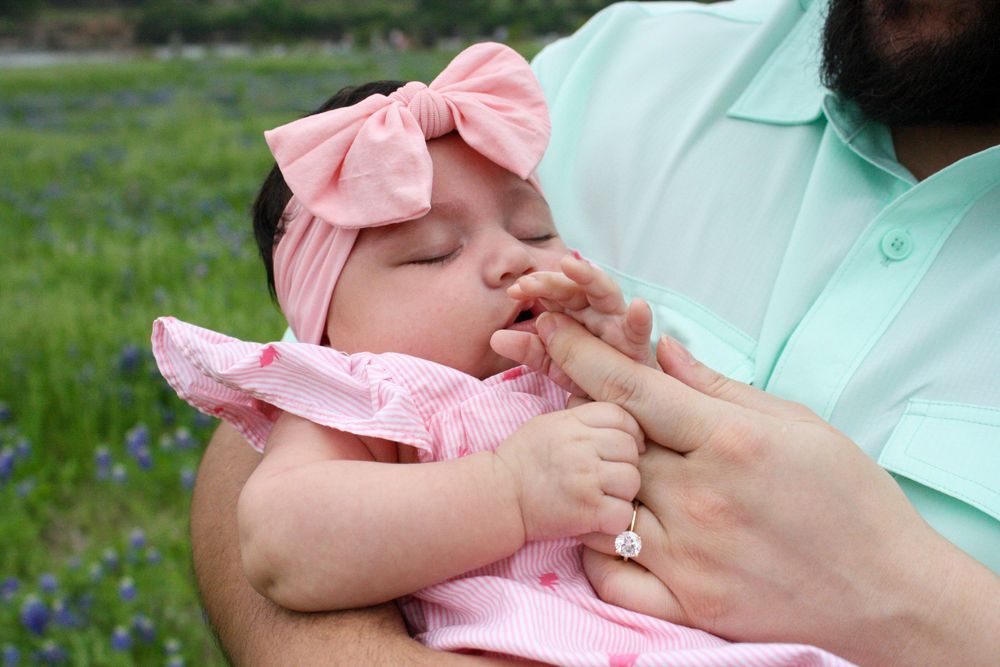 Close-up view of tiny baby hands grasping parent's fingers in outdoor setting.