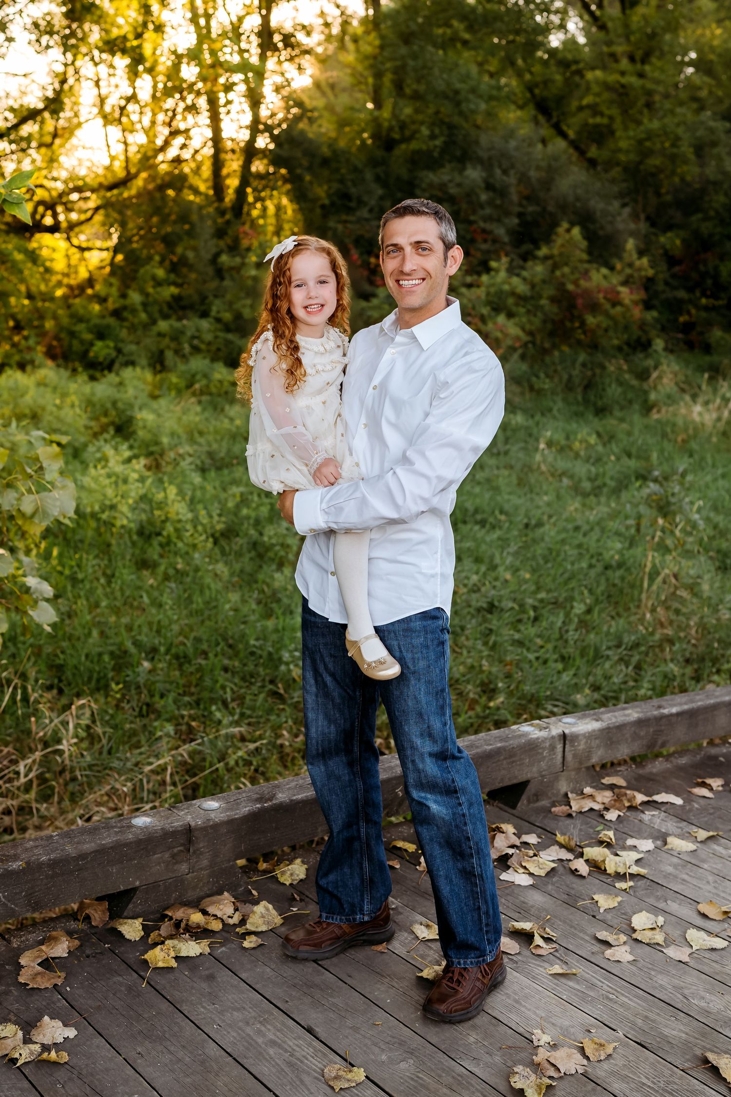 Playful family portraits on a wooden deck with autumn leaves showing a parent and child in coordinated casual outfits.