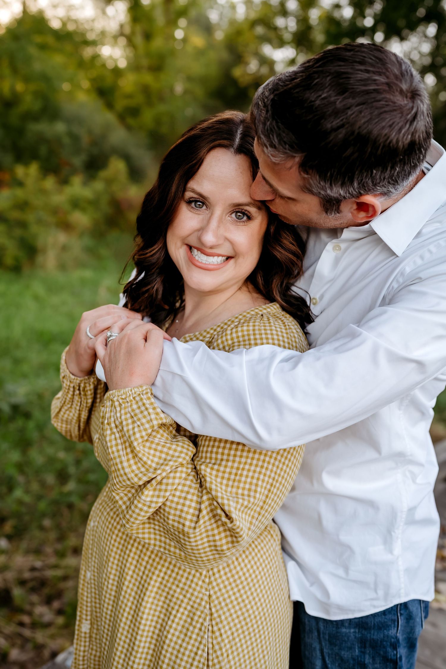 A couple in casual attire shares romantic moments outdoors during a photo session in natural lighting.