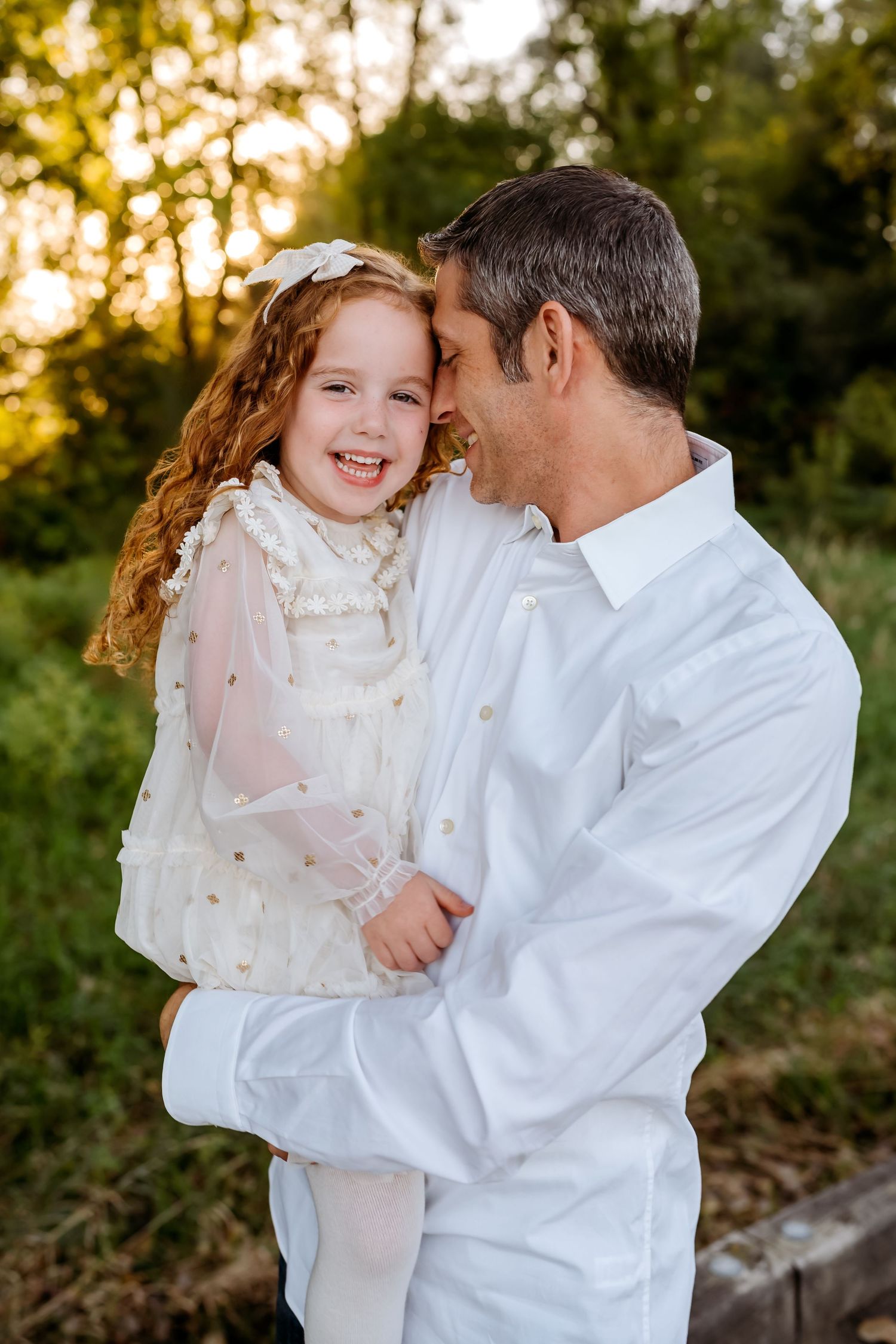 A tender moment captured at sunset between parent and child wearing white outfits against a golden backlit nature setting.