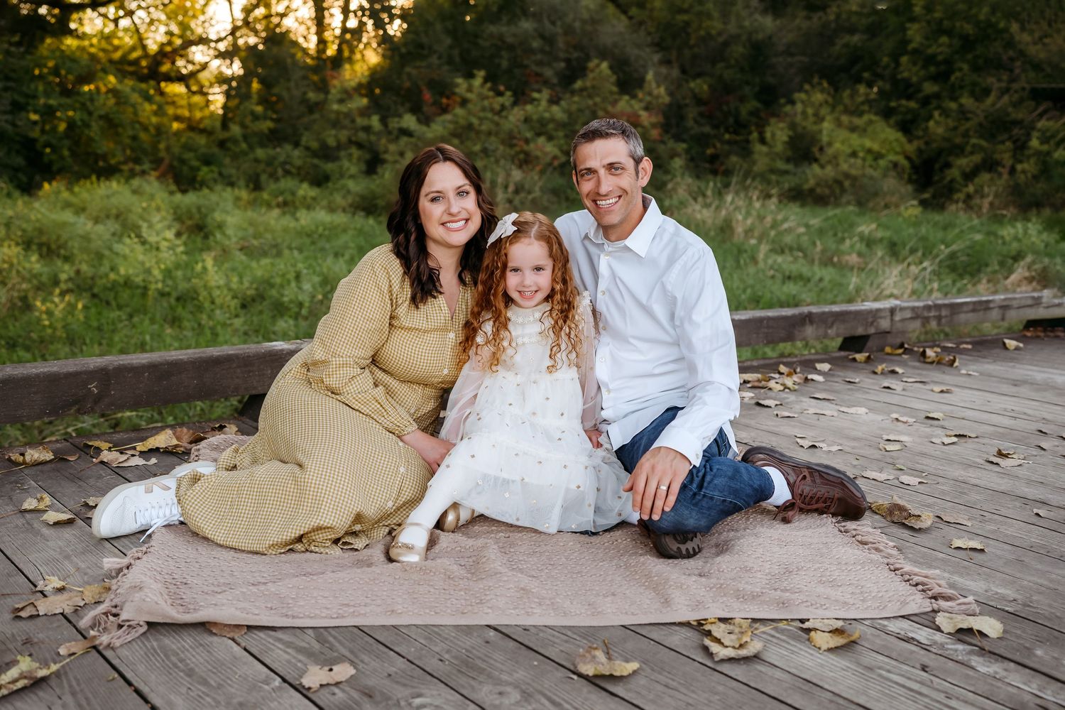 Family sits together on wooden deck during golden hour sunset in outdoor fall portrait session.