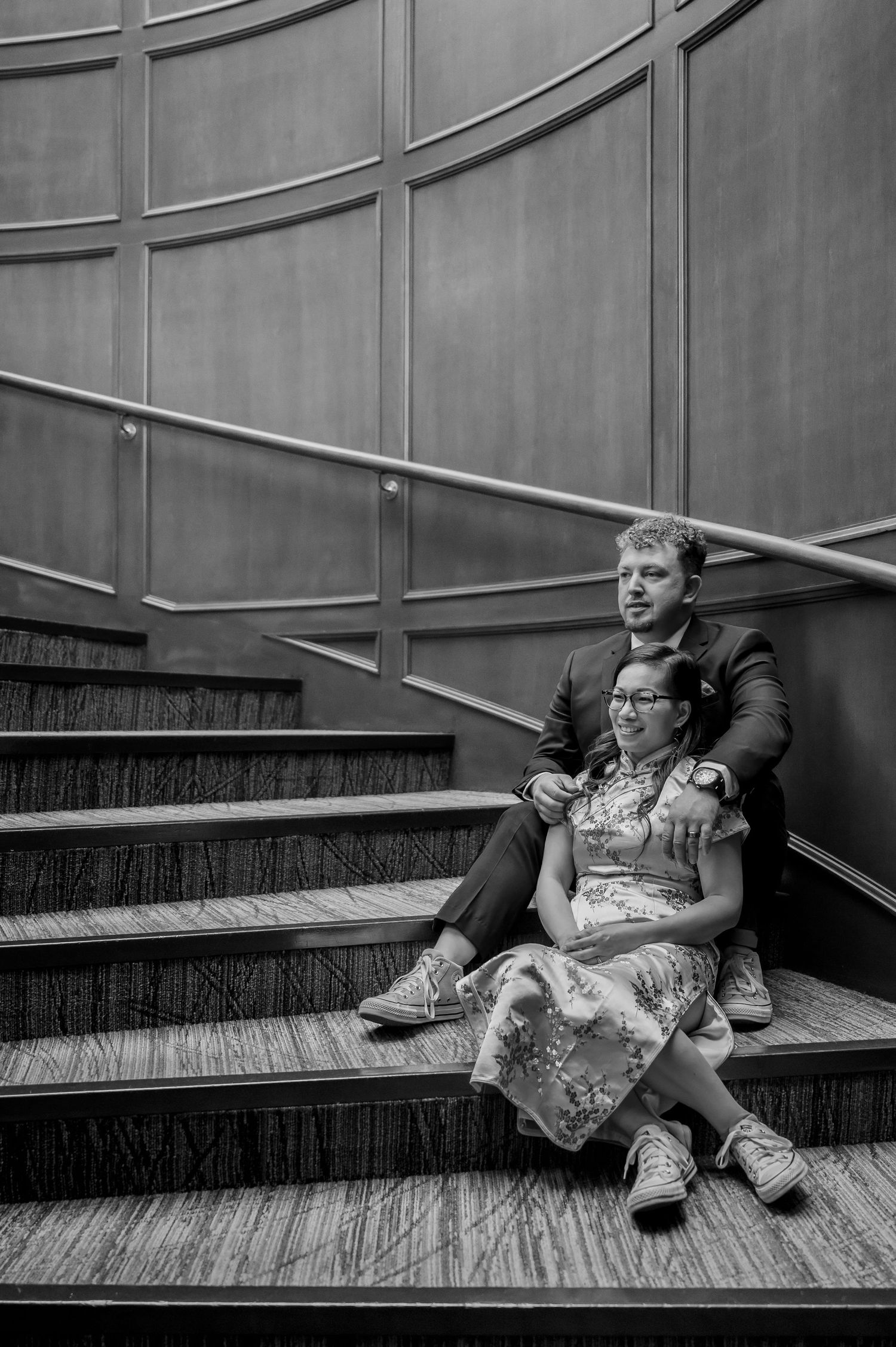 A black and white photo series showing two people sitting and reclining on wooden stairs in a modern interior space.