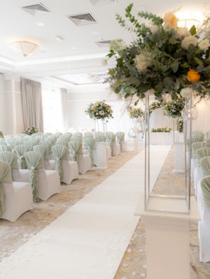 Elegant wedding ceremony venue with white chairs, tall floral arrangements, and soft lighting creating a romantic atmosphere.