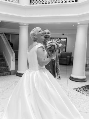 A bride in a flowing white gown poses elegantly in an ornate white interior with classical columns and marble floors.