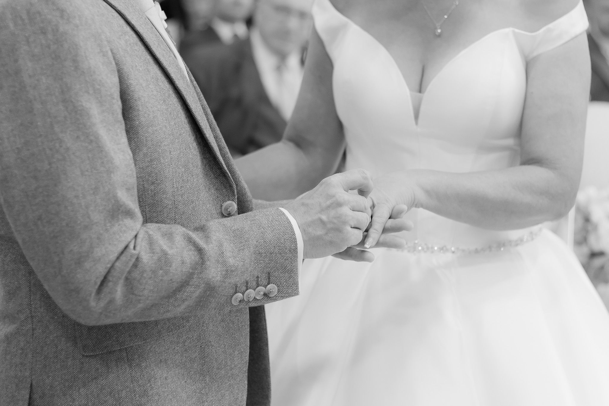 A series of black and white wedding photos showing close-up details of rings, hands, and formal attire during a ceremony.