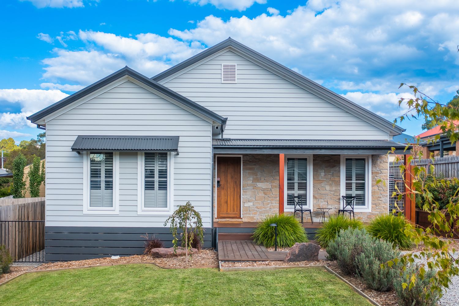 Modern grey weatherboard home with French windows, timber deck entry and established garden landscaping.