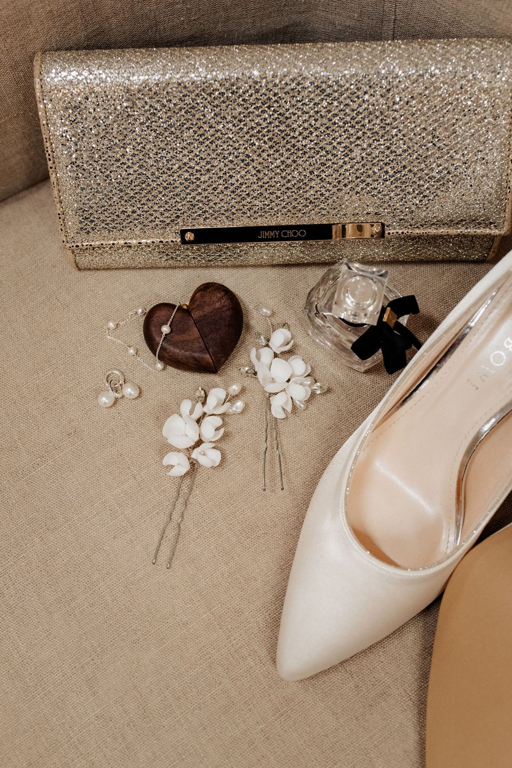 Elegant wedding accessories including beige high heels, floral hair pins, and sparkly clutch arranged on neutral background.