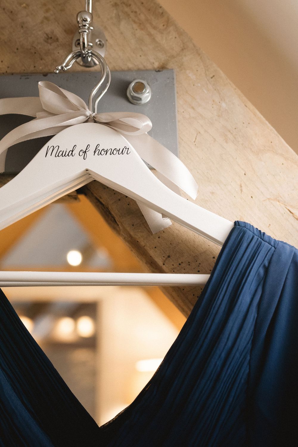 White wooden hangers labeled 'Maid of honor' display elegant navy blue bridesmaid dresses against a beige wall.