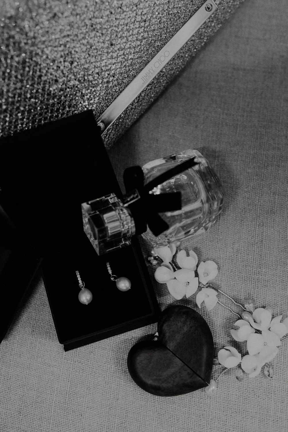 Black and white close-up sequence showing perfume bottles and flowers on a textured surface.