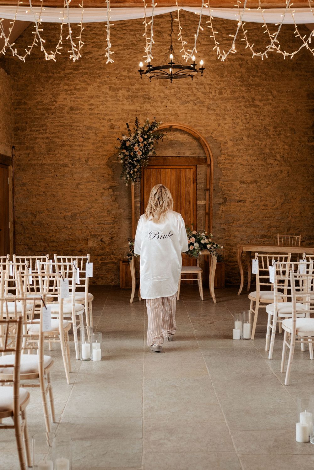Rustic brick wall wedding venue interior with white chairs arranged for ceremony and decorative floral arrangements.