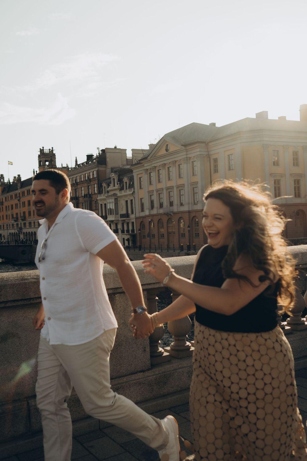 couple laughing and running through sun-lit city during romantic couples photo session in Stockholm