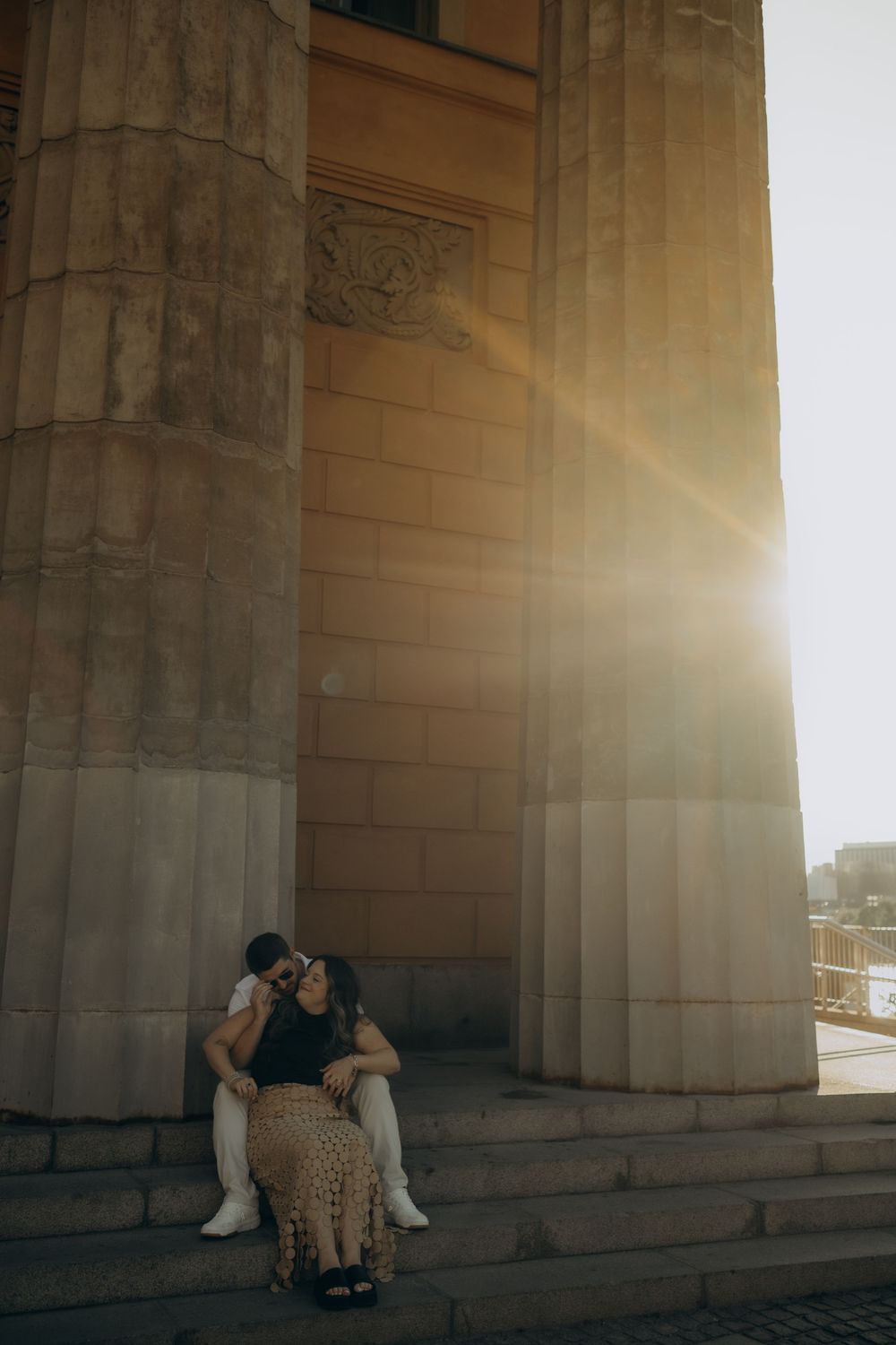 couple sitting on stairs with sunbeams in the background while being captured by the best couple photographer in Stockholm