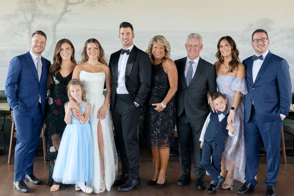 Wedding party in formal attire poses together in color photo at indoor venue.