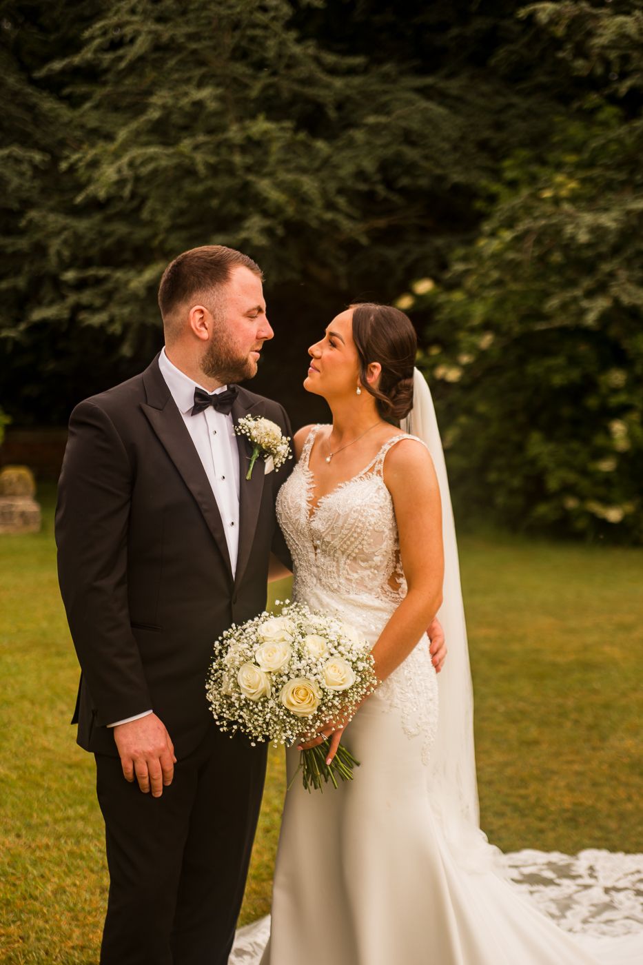 Wedding couple poses together against a natural backdrop with bride holding baby's breath bouquet.
