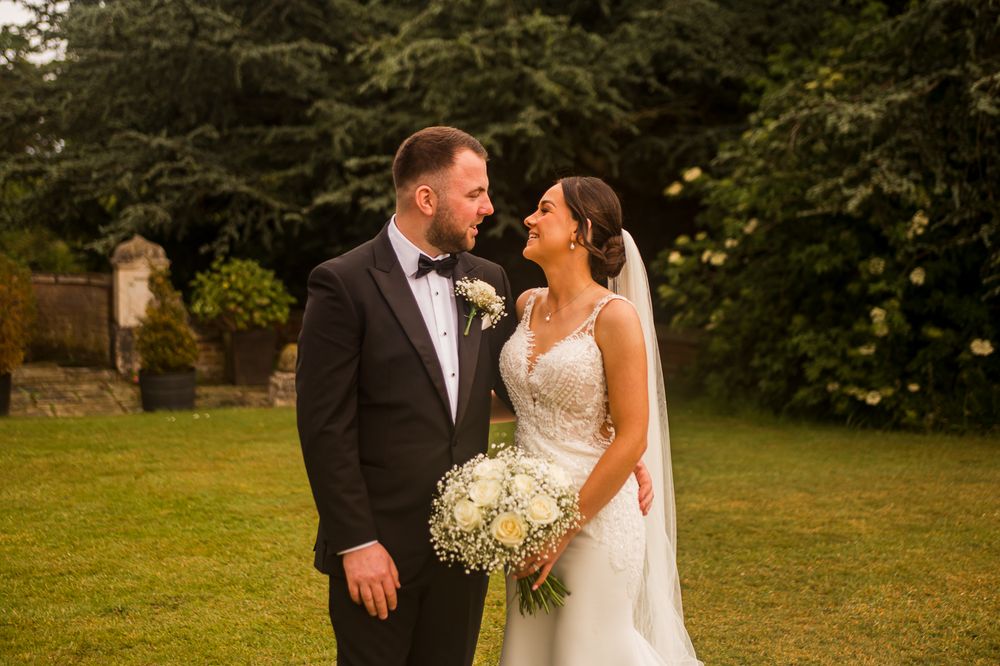 Romantic outdoor wedding photography session with couple in formal attire on grassy lawn.