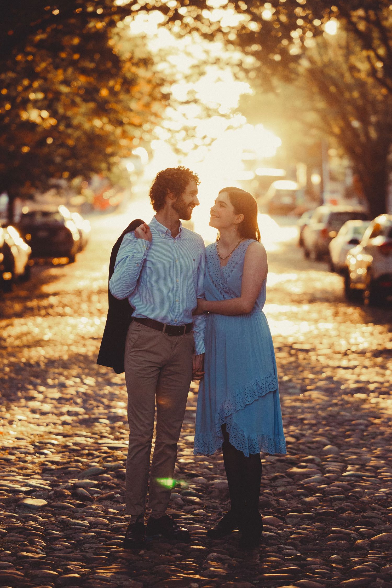 A couple walks together on a leaf-covered path during golden hour sunset with warm autumn lighting.