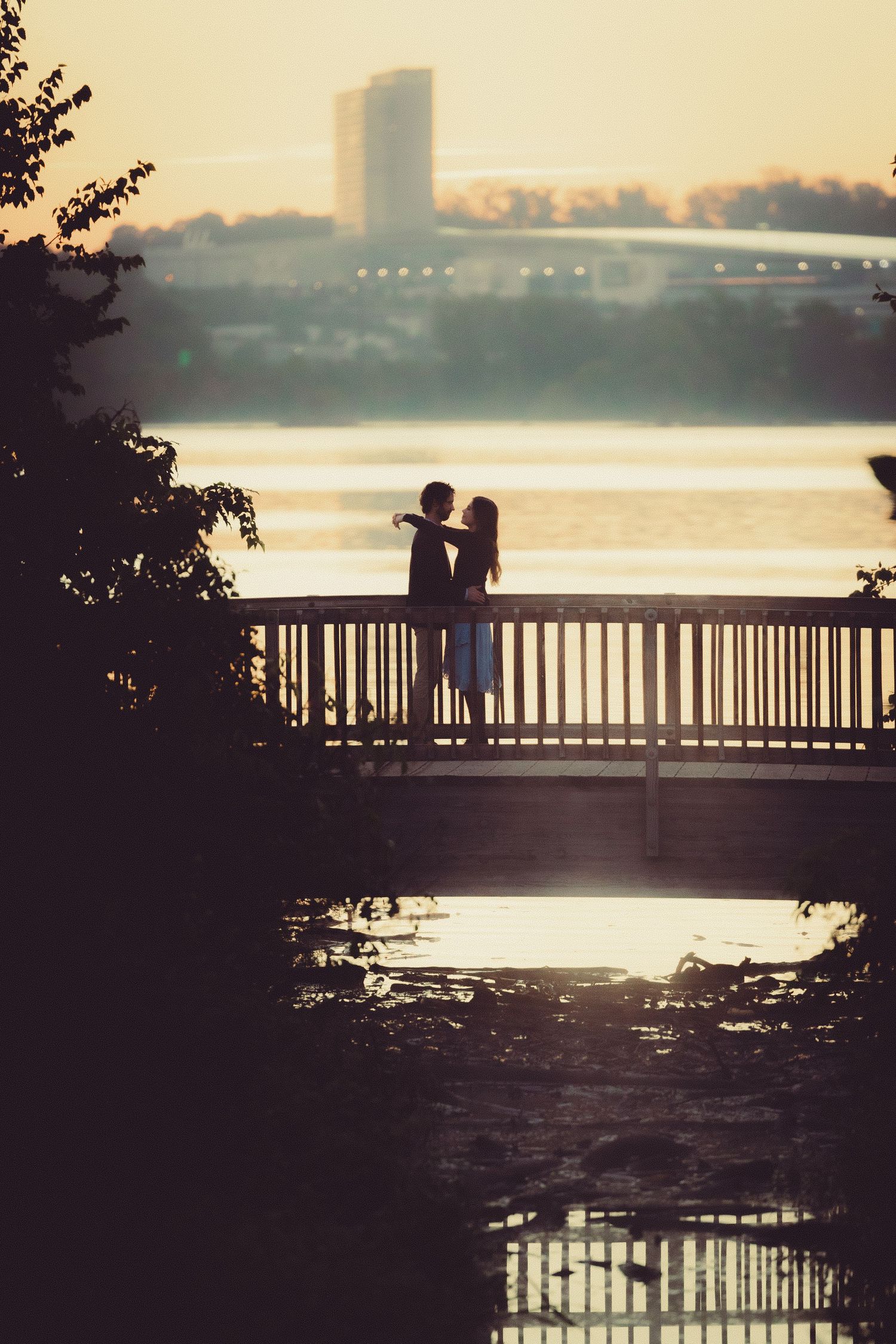 Warm film-style portrait of couple embracing by the Potomac River at sunrise