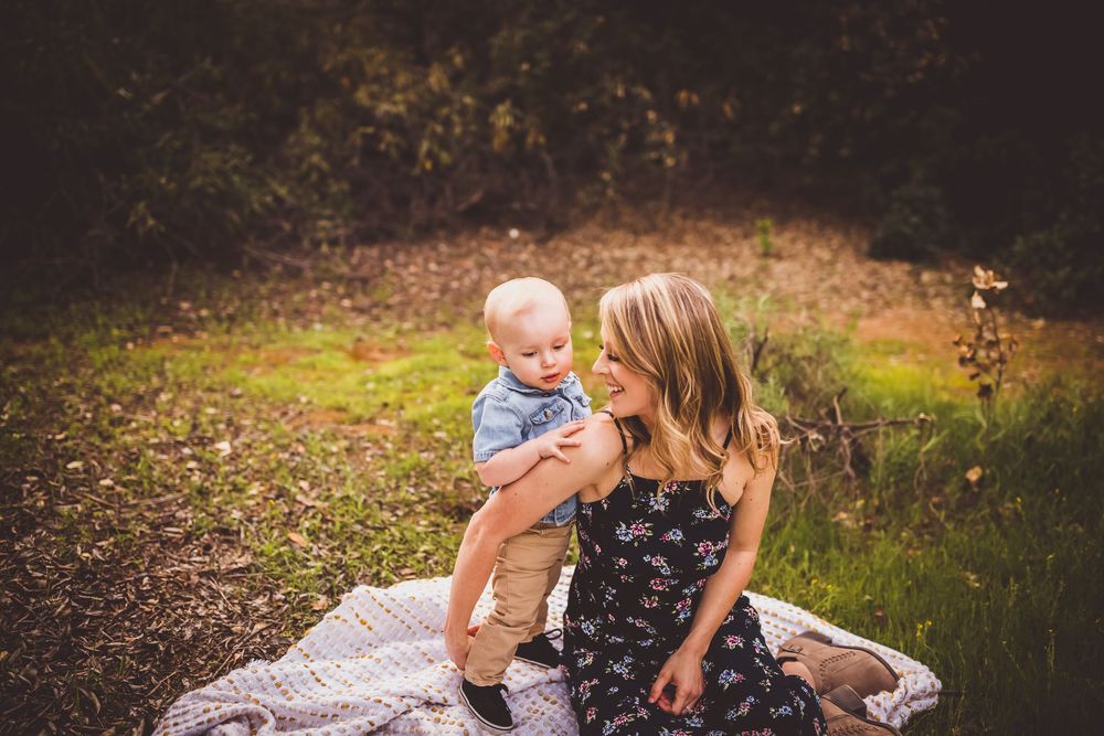 A mother and baby share a tender moment outdoors on a blanket during a family photoshoot.