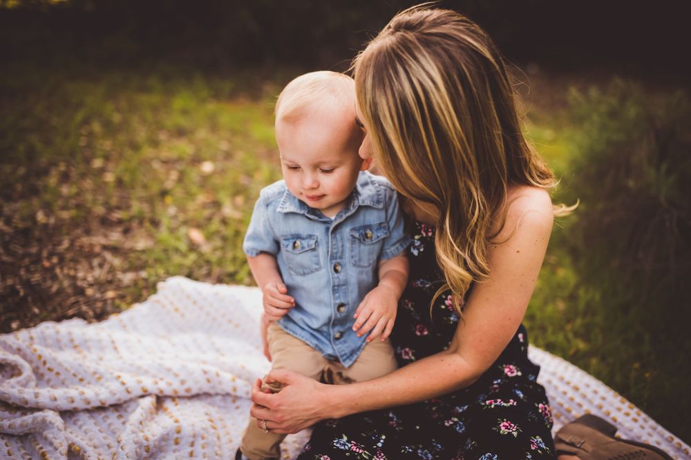 A mother and child sit together on a blanket in a natural outdoor setting during golden hour.
